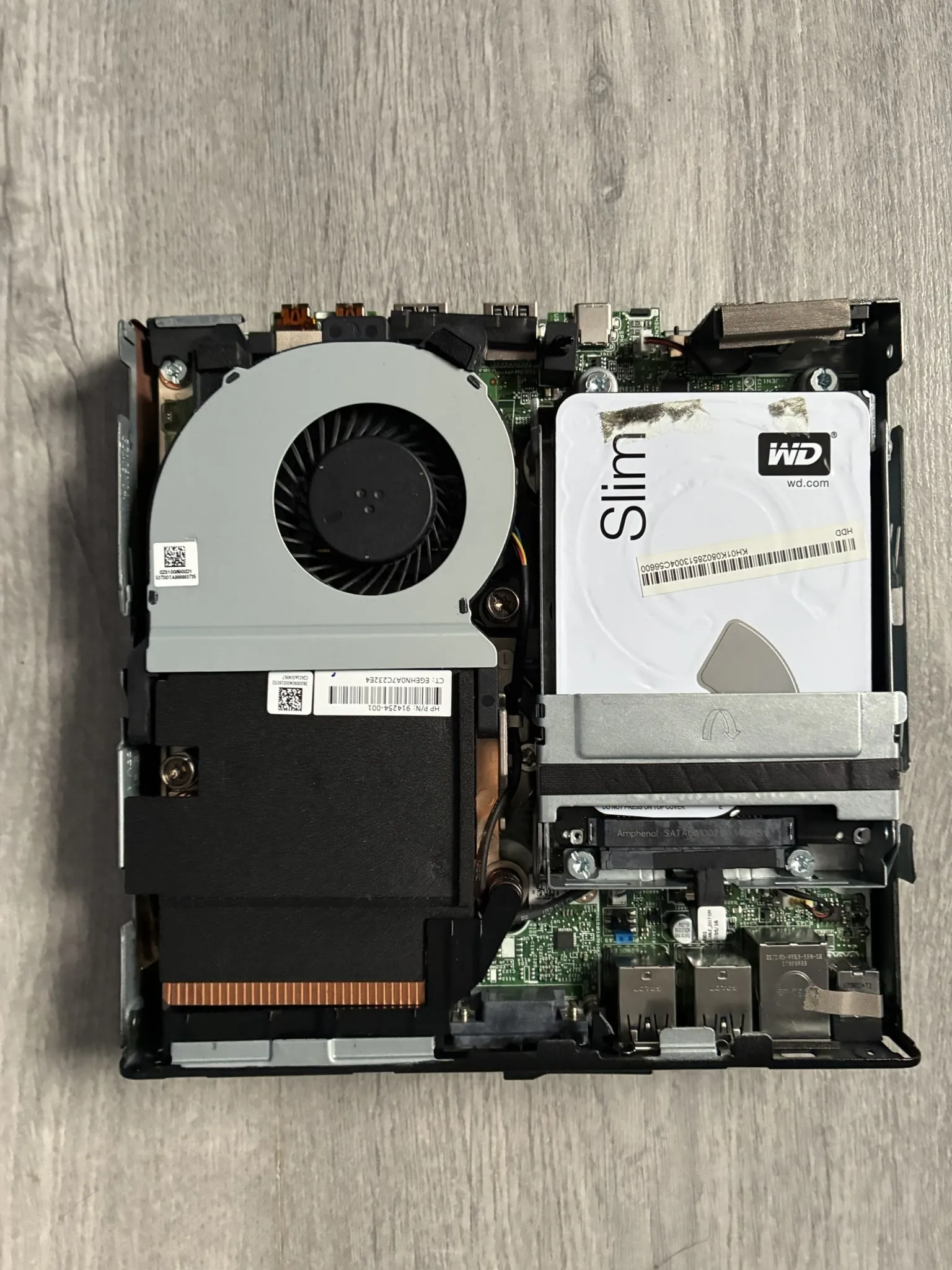 Interior of the HP EliteDesk mini PC with its case open, showing the cooling fan, a 2.5-inch hard drive and the compact motherboard